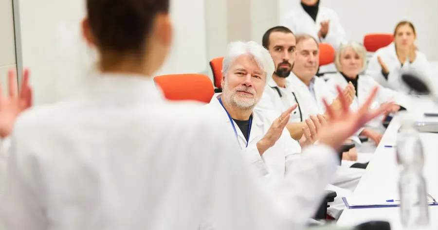 Ακροατήριο γιατρών χειροκροτεί τον ομιλητή σε ιατρική ημερίδα — Ποια είναι η καλύτερη αστική ευθύνη ιατρών