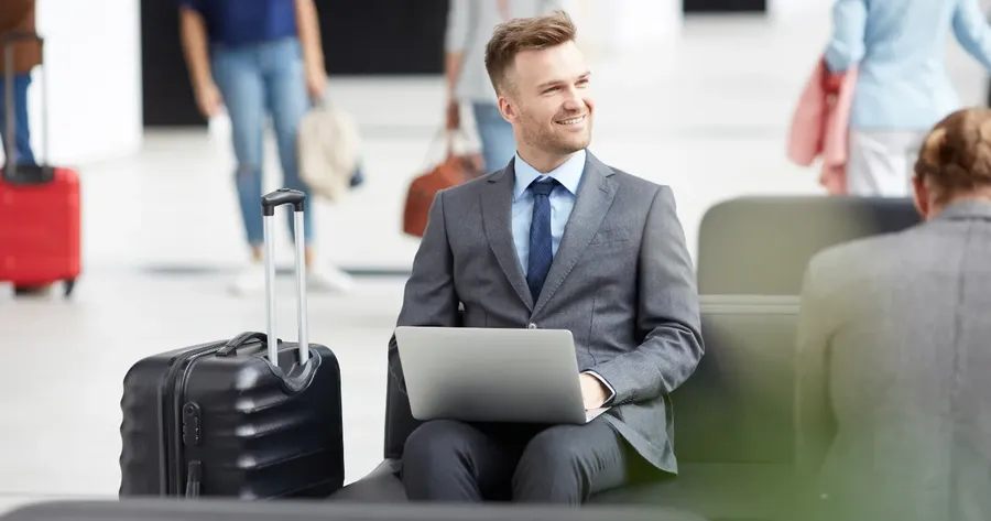 επαγγελματίας με κοστούμι, laptop και βαλίτσα σε lounge αεροδρομίου — Ασφάλιση Επαγγελματικών Ταξιδιών